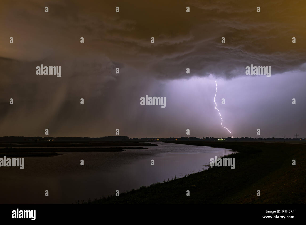 Omnious Himmel und Leistungsstarker Blitz mit einem regen Welle, um die in der Nähe von einem See in Holland. Während eines Sturms Chase, in der Nähe von Rotterdam fotografiert. Stockfoto