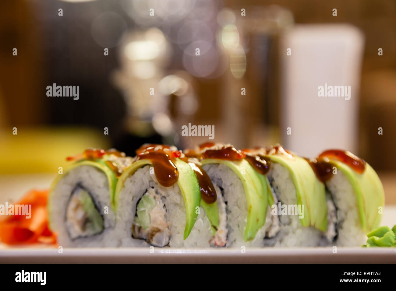 Closeup Shogun Sushi Roll mit Avocado, Erdbeere, teriyaki Sauce, Sesam, Wasabi, Ingwer, weisse japanische Platte, Sojasauce, weiße Servietten, Glas ... Stockfoto