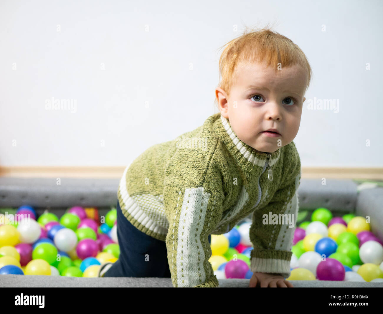 Niedlichen kleinen 2 jährigen Jungen glücklich aber müde allein mit bunten Bällen zu spielen und klettert aus Ball Pool Indoor Spielplatz Zimmer Nahaufnahme mit viel Stockfoto