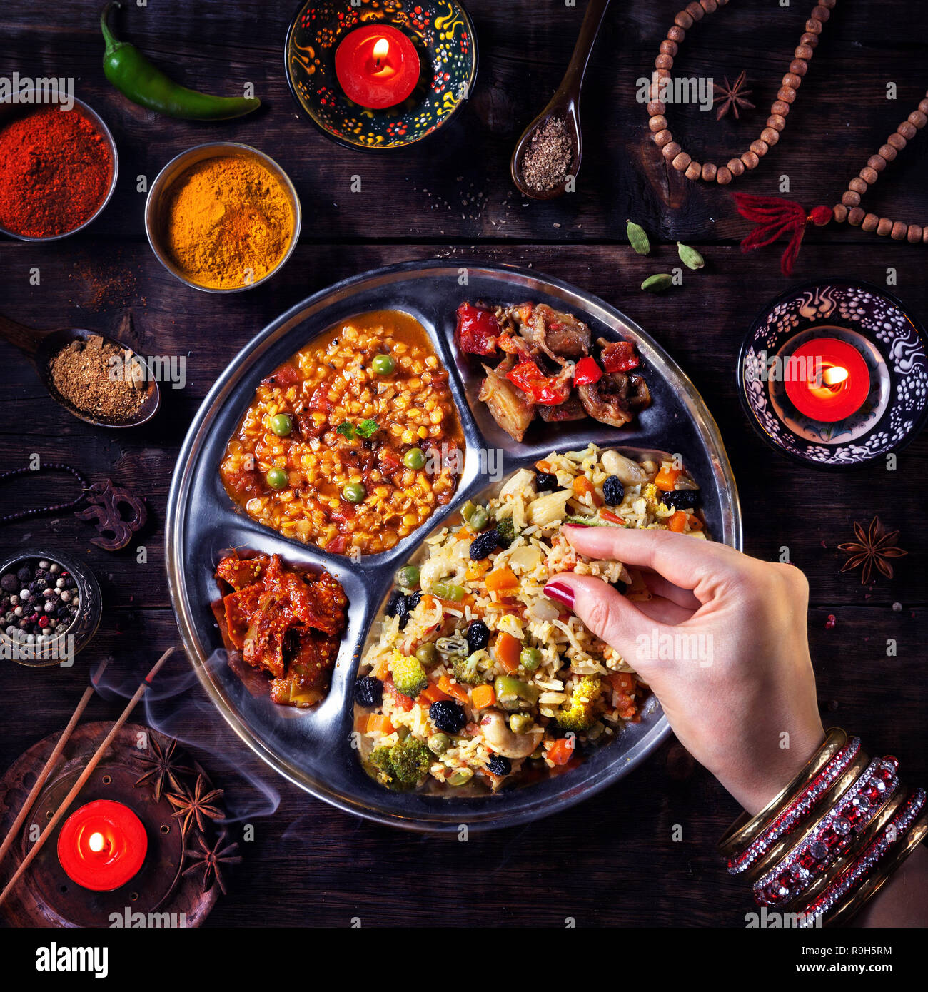 Frau essen Vegetarische biryani durch ihre Hand mit Armreifen in der Nähe von Kerzen, Weihrauch und religiöse Symbole in Diwali Feier Stockfoto
