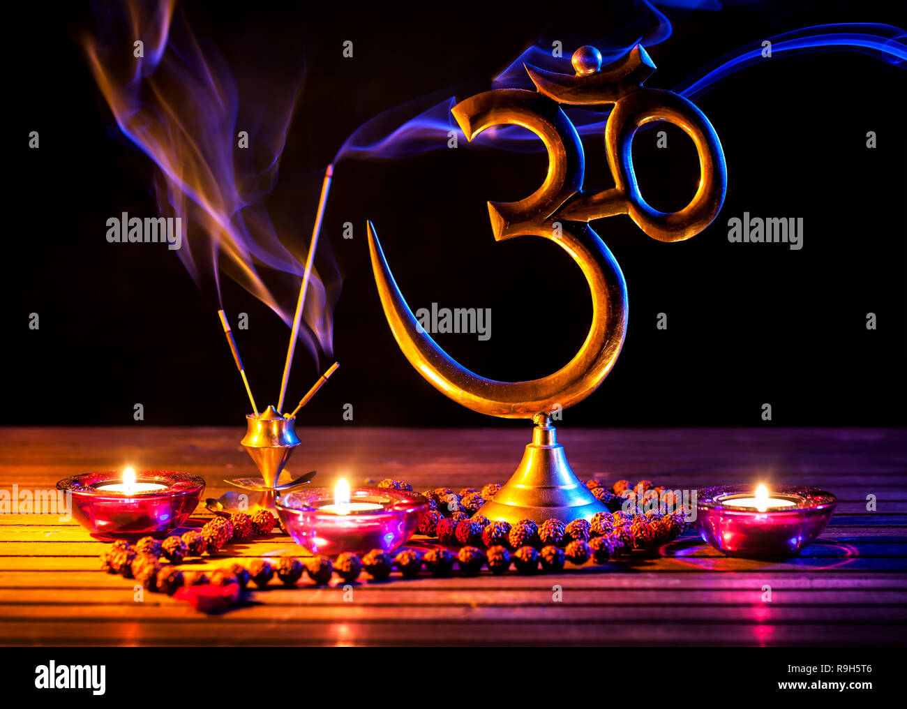 Om Symbol, Weihrauch Rauch, Kerze und japa Mala auf Holztisch auf schwarzem Hintergrund Stockfoto