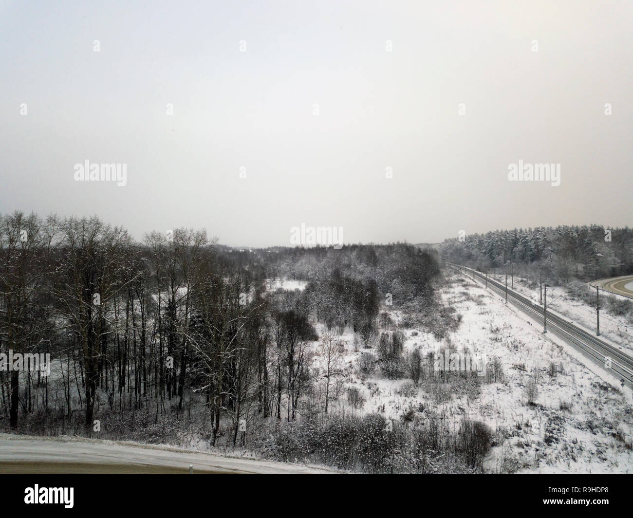 Panoramablick auf das Luftbild von einer Eisenbahn durch die verschneiten Wälder und Felder Stockfoto