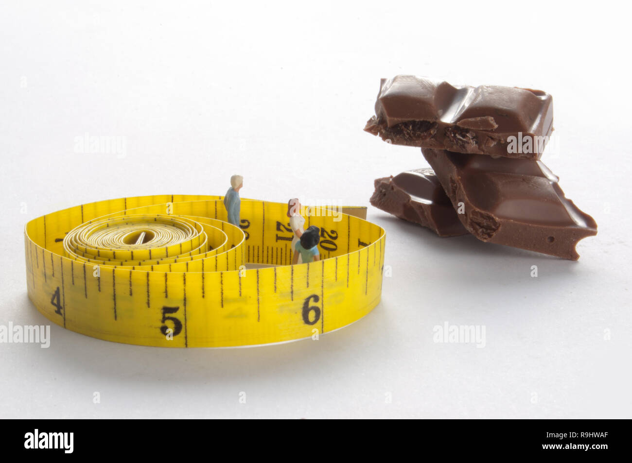 Miniatur Personen innerhalb ein Maßband mit Blick auf einen Stapel von Schokolade Blöcke Stockfoto
