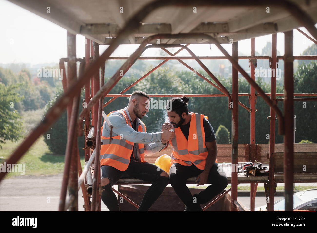 Zwei glückliche Männer lachen bei der Arbeit in der Baustelle. Team der Arbeitnehmer rauchen Zigarette und Sprechen während der Pause Stockfoto