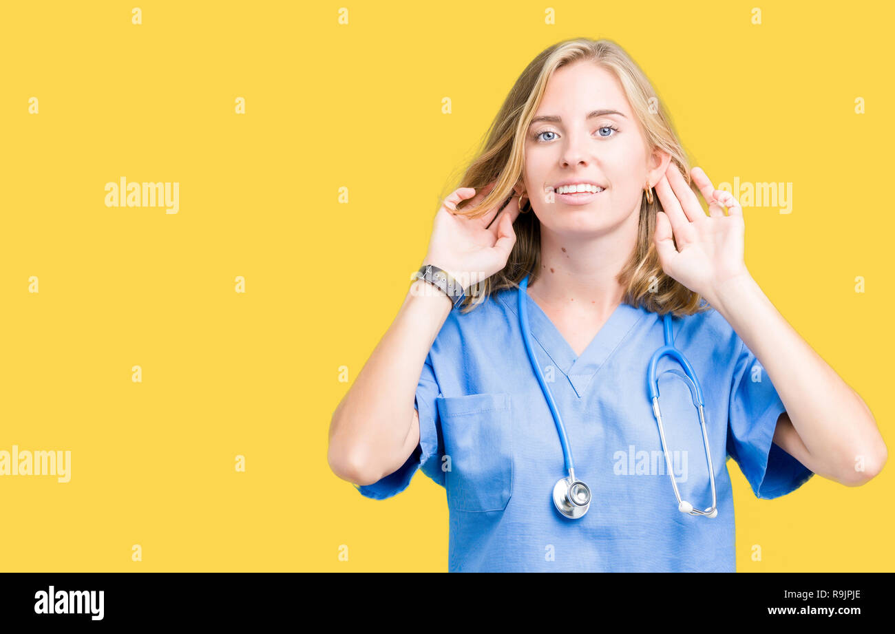 Schöne junge Arzt Frau mit medizinischen gleichmäßig über isolierte Hintergrund versuchen, beide Hände am Ohr Geste zu hören, neugierig, für Klatsch und Tratsch. Anhörung pr Stockfoto