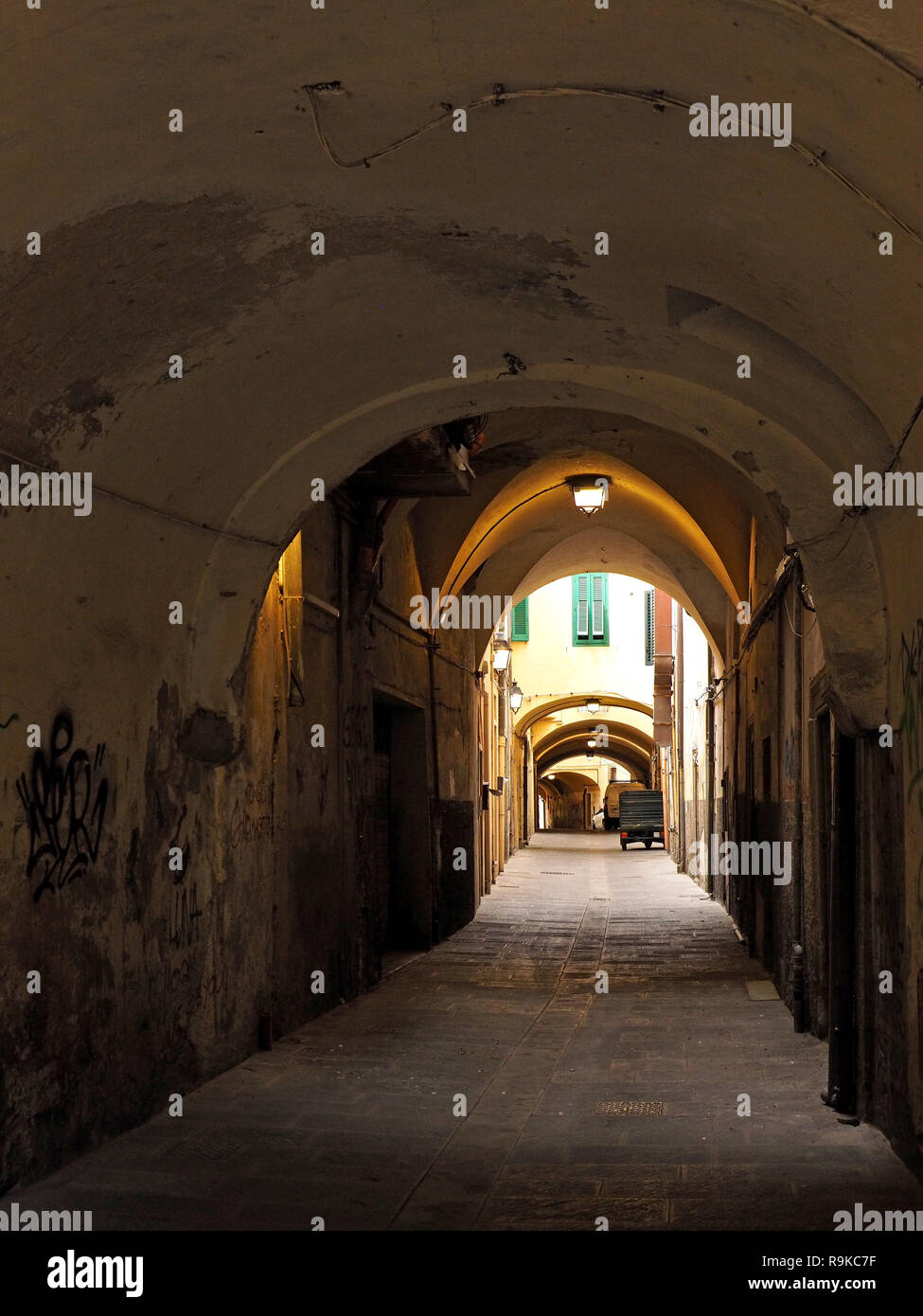 Typische Gasse mit schattigen gewölbten Bögen und grünen Fensterläden im Sonnenlicht in Pisa, Italien Stockfoto