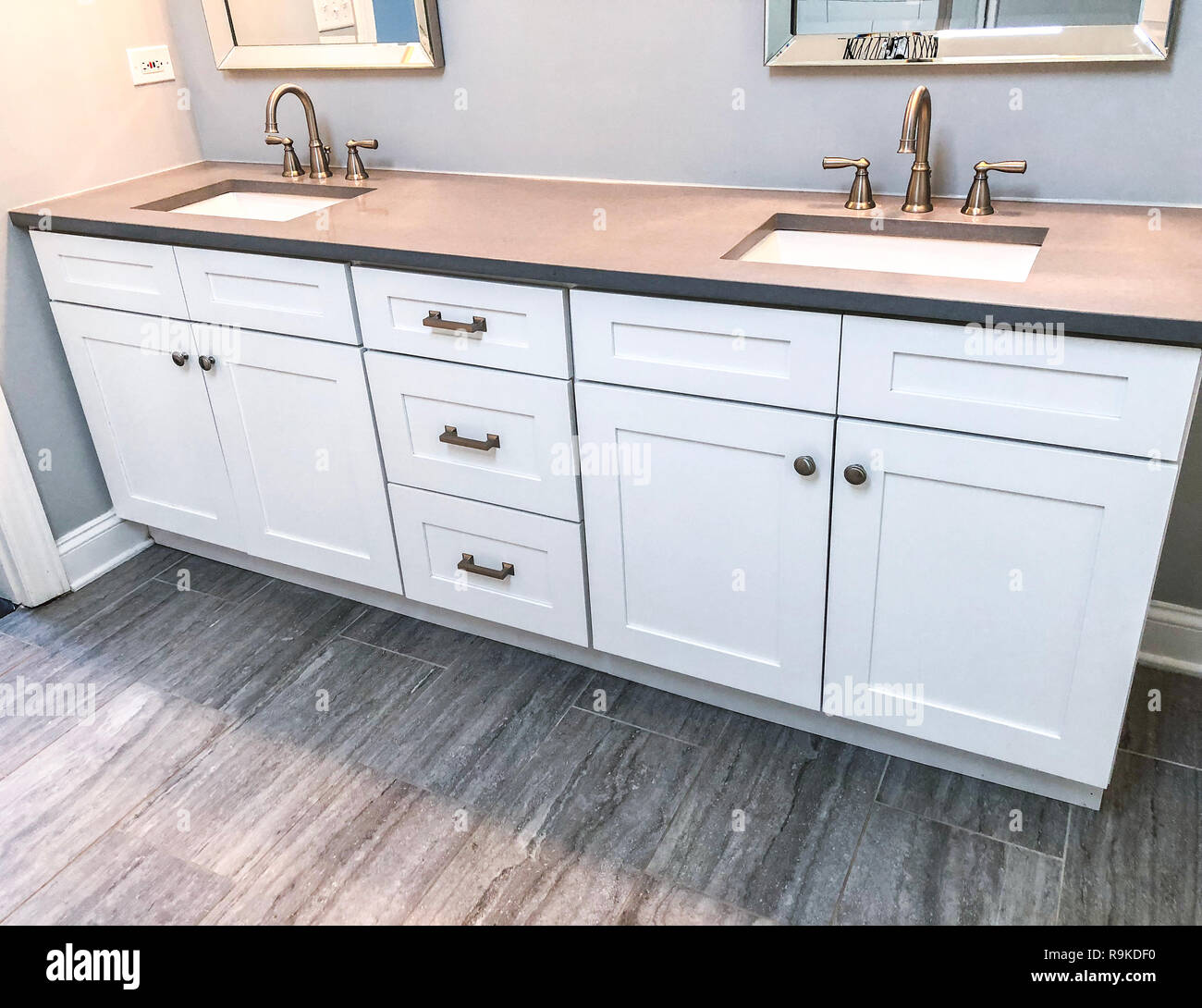 Moderne Badezimmer-Innenausstattung der weißen Shaker-Schränke, Granit-Arbeitsplatte, zwei weiße Waschbecken und Porzellanfliesen Stockfoto