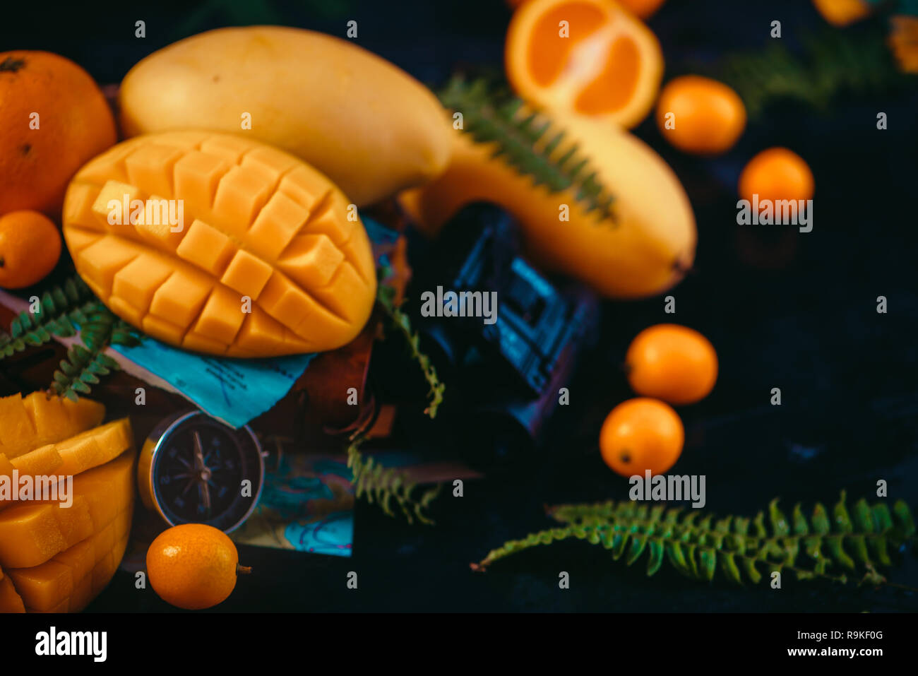 Cut mango Hälften close-up Header mit Orangen, kumquat und andere tropische Früchte. Der dunkle Hintergrund mit kopieren. Entdeckung von exotischen Früchten Konzept Stockfoto