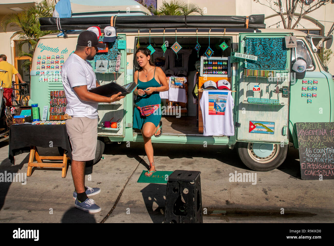 Eine junge Frau veteran Reisende in einem Huntington Beach, CA, Street Festival Exponate der Volkswagen Van, in dem Sie fuhr 40.000 Meilen von Argentinien nach Alaska zusammen mit Erinnerungen an ihre Reise zum Verkauf einschließlich ein T-Shirt. Stockfoto