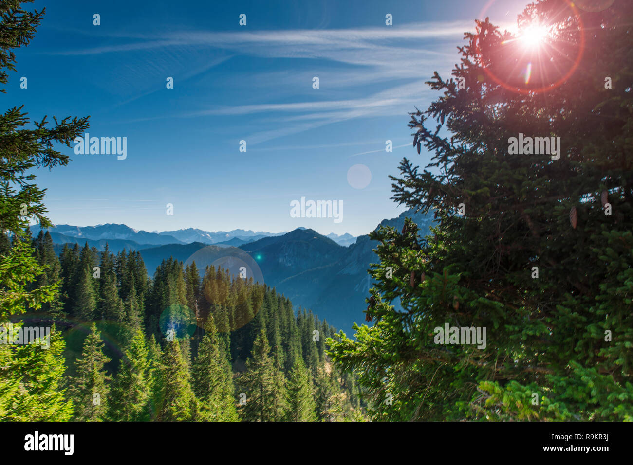 Blick gegen die Sonne über einem Tal am Tegelberg in Bayern auf die angrenzende Berglandschaft der Alpen in Richtung Österreich im Sommer mit Blau Stockfoto