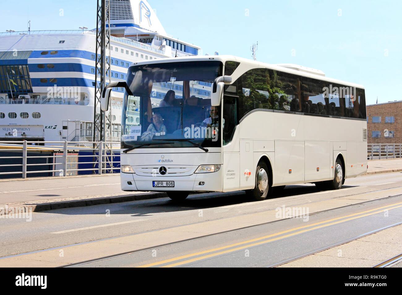 Helsinki, Finnland - 24. Mai 2018: Weiße Mercedes-Benz Bus fährt Sea Port an einem sonnigen Tag des Sommers mit Passagieren an Bord der Fähre auf dem Hintergrund. Stockfoto