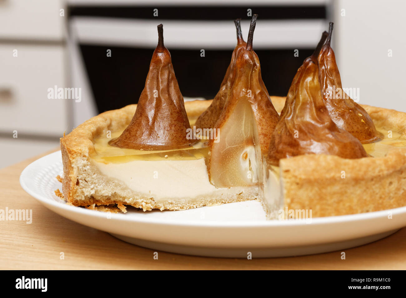 Pear-Kuchen mit Sahne Butter und Marmelade mit abgeschnitten Stücke auf hölzernen Tisch gegen verwackelte Küche Hintergrund Stockfoto