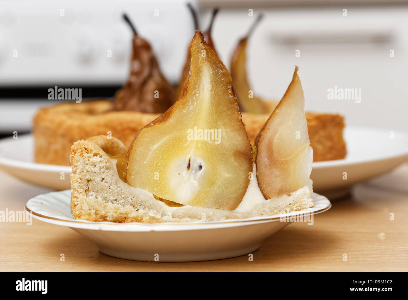 Stück der Torte mit Birnen, Sahne Butter und Marmelade auf hölzernen Tisch gegen verwackelte Küche Hintergrund Stockfoto