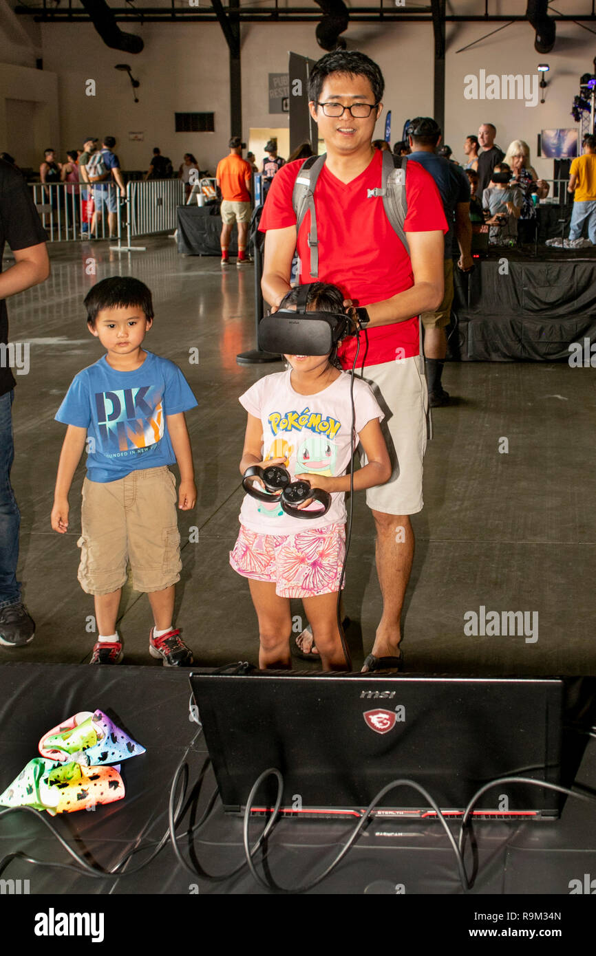 Von ihrem Vater begleitet, eine asiatische American Girl zieht ein Virtual reality Headset ein Computer Spiel bei einem Elektronik Festival in Costa Mesa, CA zu spielen. Ihr kleiner Bruder scheint nicht beeindruckt zu werden. Stockfoto