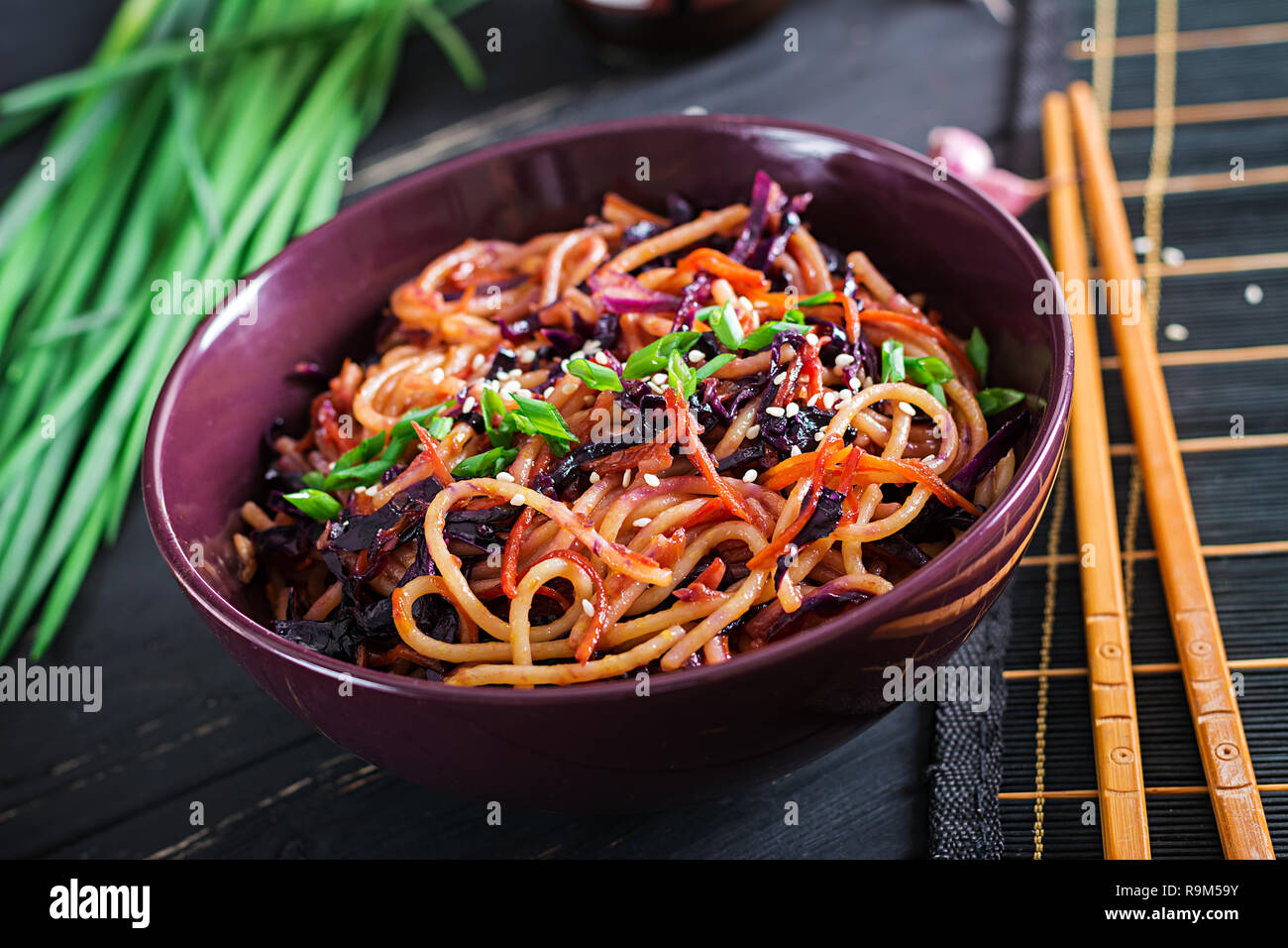 Chinesisches Essen. Vegan fry Nudeln mit Rotkohl und Karotten in einer Schüssel verrühren auf schwarzem Holz- Hintergrund. Asiatische Küche essen. Stockfoto