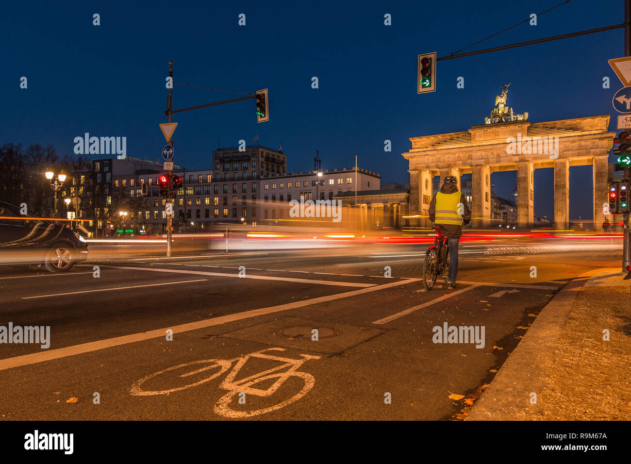 Brandenburger Tor bei Nacht. Rückseite Blick auf der Straße mit Radfahrern und Licht der Autos an Langzeitbelichtung. Radweg mit Vorzeichen auf dem Asphalt. Stockfoto