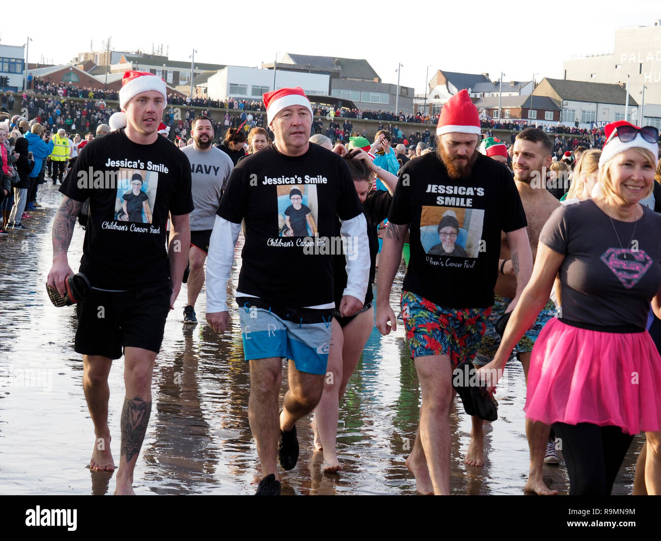 Redcar Cleveland England 26. Dezember 2018. Die jährlichen Boxing Day Liebe 'ip' wurde heute in ungewöhnlich mildes Wetter mit Massen von Menschen an und mit der Rnli und Küstenwache schauen für Sicherheit am Strand in Redcar während, wenn Leute in Fancy Dress gehen in die Nordsee für Spaß und Geld für ihre Nächstenliebe zu heben. Hier drei Männer unterstützen, Jessicas Smile Kinder Krebs Fonds Credit: Peter Jordan_NE/Alamy leben Nachrichten Stockfoto