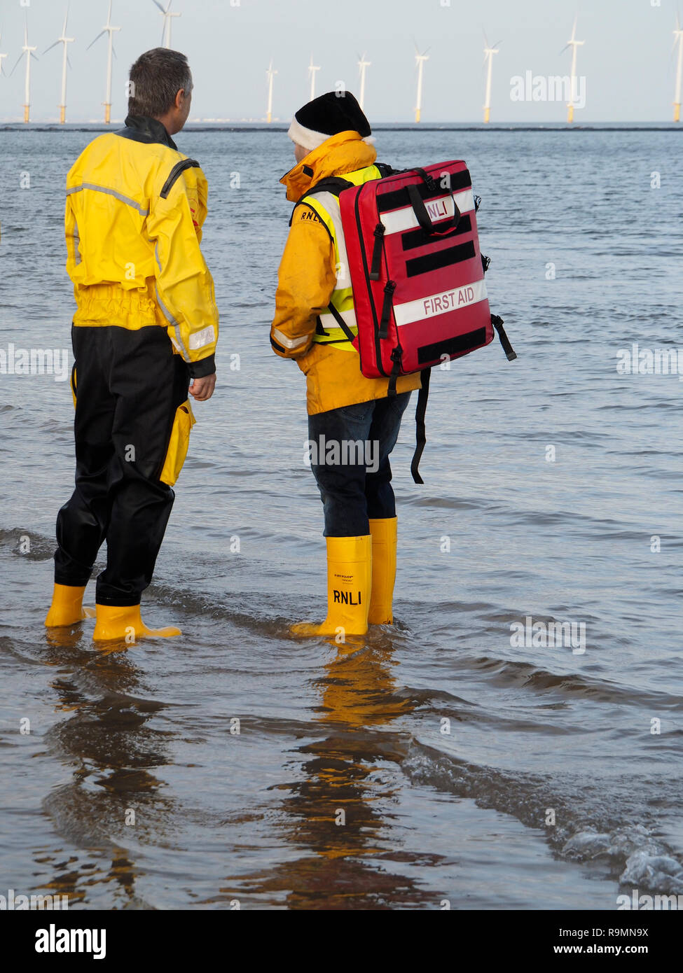 Redcar Cleveland England 26. Dezember 2018. Die jährlichen Boxing Day Liebe 'ip' wurde heute in ungewöhnlich mildes Wetter mit Massen von Menschen an und mit der Rnli und Küstenwache schauen für Sicherheit am Strand in Redcar während, wenn Leute in Fancy Dress gehen in die Nordsee für Spaß und Geld für ihre Nächstenliebe zu heben. Hier zwei rettungsbootleute stehen im flachen Wasser, einer trägt einen Erste Hilfe Rucksack Credit: Peter Jordan_NE/Alamy leben Nachrichten Stockfoto