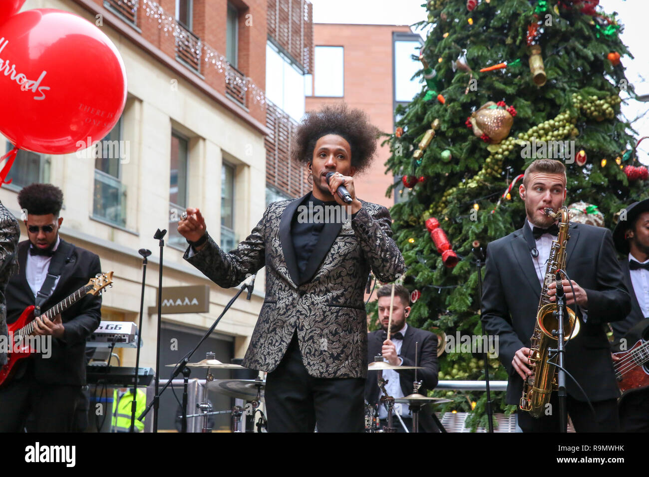 Harrods Soul Band gesehen der Unterhaltung der Käufer, da sie außerhalb des Luxus Kaufhaus Harrods in Knightsbridge vor der Öffnung der Boxing Day verkauf Warteschlange. Boxing Day ist einer der hektischsten Tage für den Einzelhandel mit Tausenden von potenziellen Kunden die Vorteile der Post - Weihnachten Schnäppchen. Stockfoto