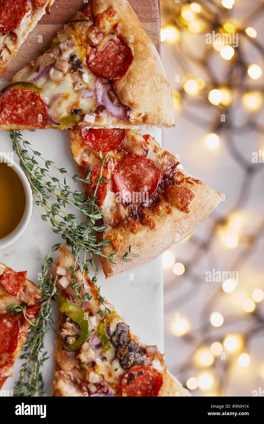 Weihnachten und Neujahr Atmosphäre. Heiße italienische Pizza mit Schmelzen mit Tomate, Salami und Käse auf einem weißen Marmor Schneidebrett. Hintergrund mit Beleuchtung Stockfoto