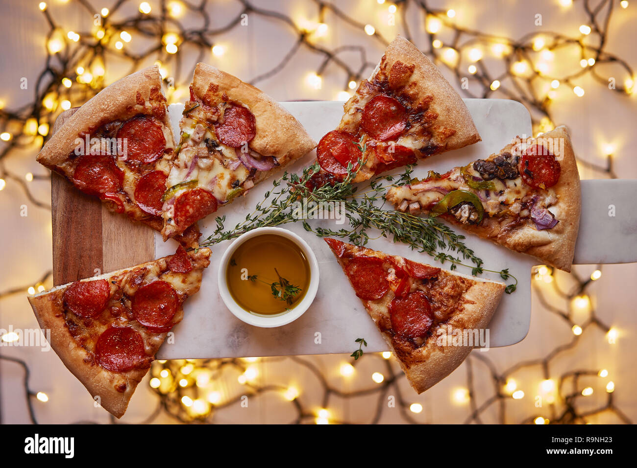 Weihnachten und Neujahr Atmosphäre. Heiße italienische Pizza mit Schmelzen mit Tomate, Salami und Käse auf einem weißen Marmor Schneidebrett. Hintergrund mit Beleuchtung Stockfoto