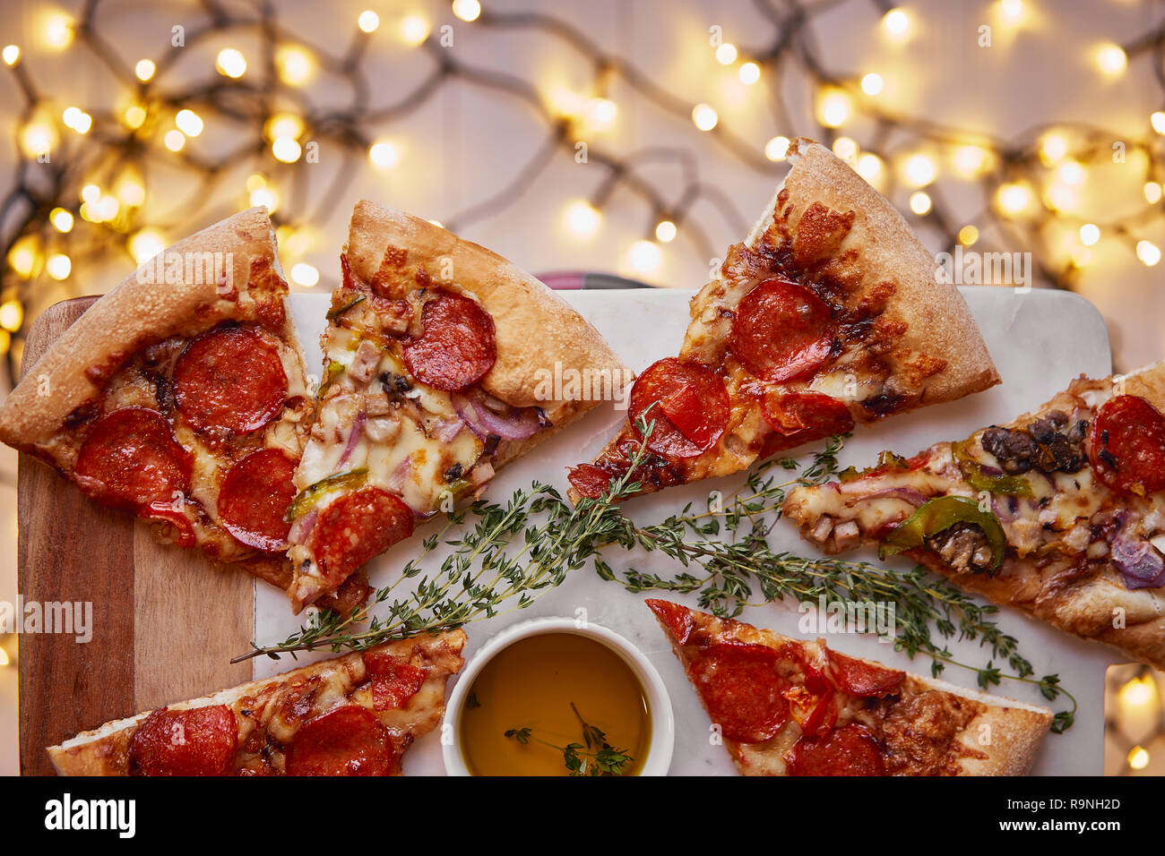 Weihnachten und Neujahr Atmosphäre. Heiße italienische Pizza mit Schmelzen mit Tomate, Salami und Käse auf einem weißen Marmor Schneidebrett. Hintergrund mit Beleuchtung Stockfoto