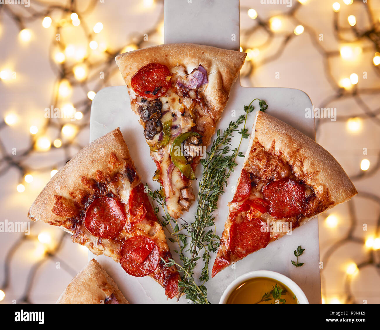 Weihnachten und Neujahr Atmosphäre. Heiße italienische Pizza mit Schmelzen mit Tomate, Salami und Käse auf einem weißen Marmor Schneidebrett. Hintergrund mit Beleuchtung Stockfoto