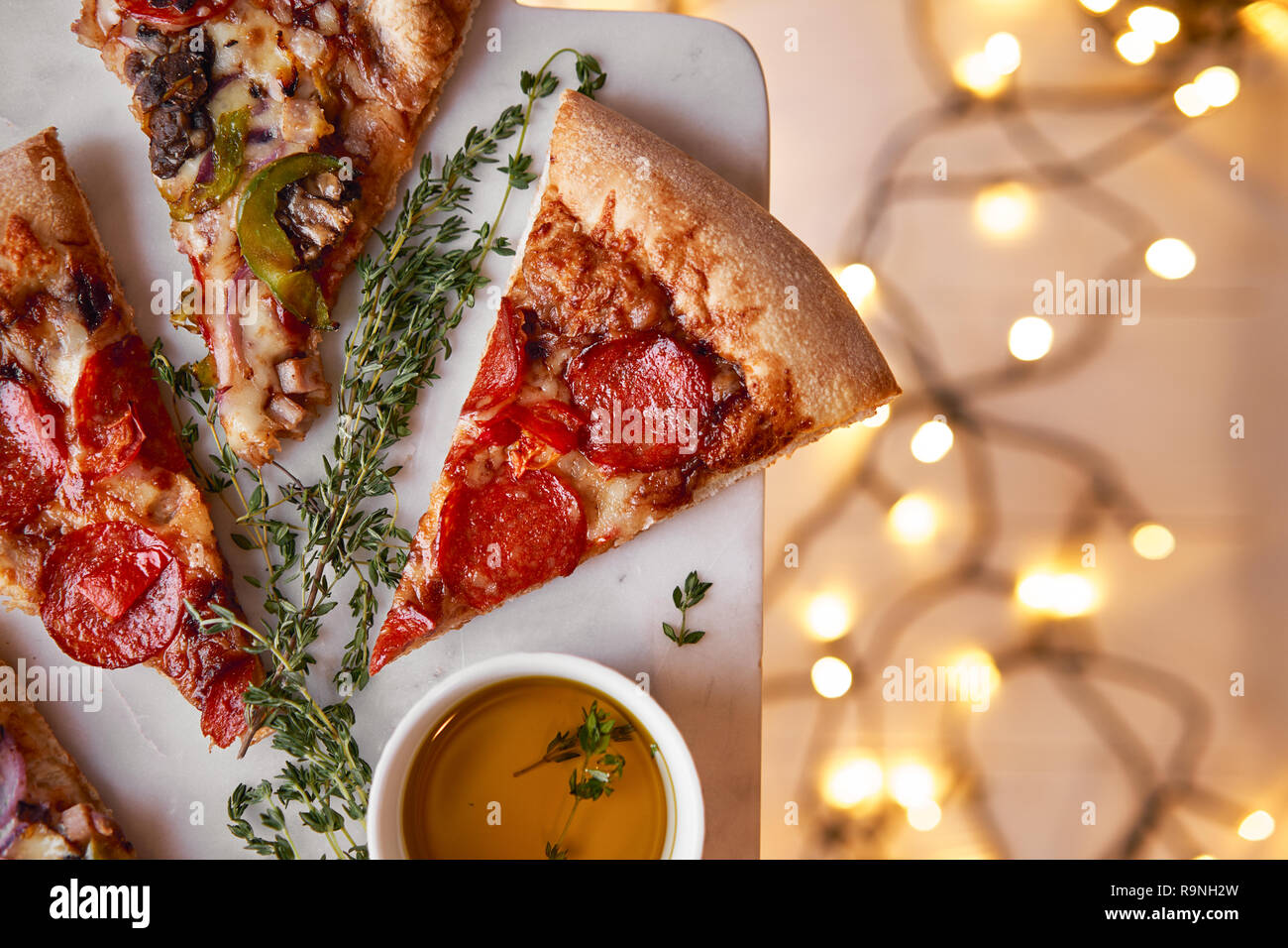 Weihnachten und Neujahr Atmosphäre. Heiße italienische Pizza mit Schmelzen mit Tomate, Salami und Käse auf einem weißen Marmor Schneidebrett. Hintergrund mit Beleuchtung Stockfoto