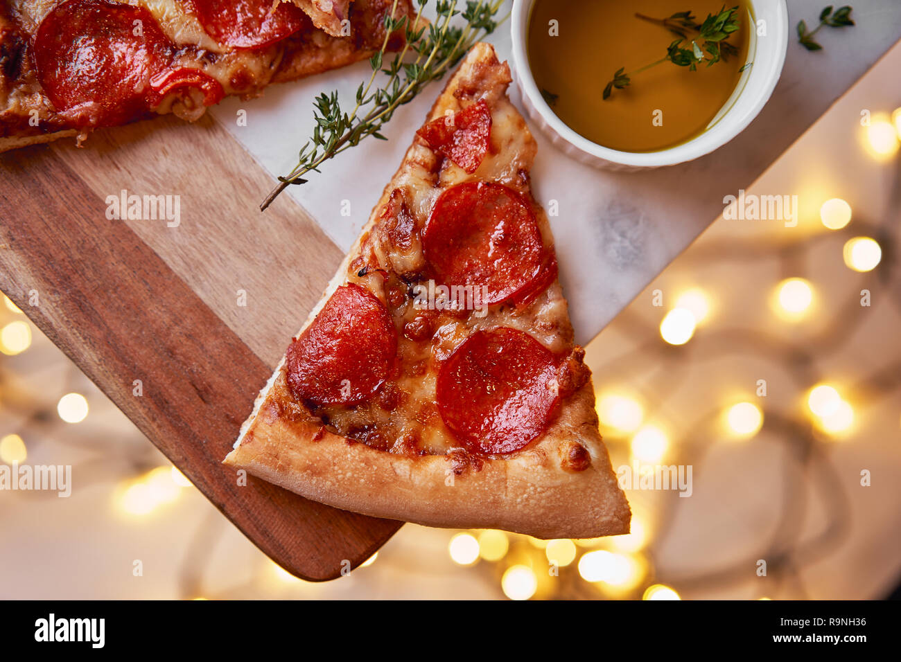 Weihnachten und Neujahr Atmosphäre. Heiße italienische Pizza mit Schmelzen mit Tomate, Salami und Käse auf einem weißen Marmor Schneidebrett. Hintergrund mit Beleuchtung Stockfoto