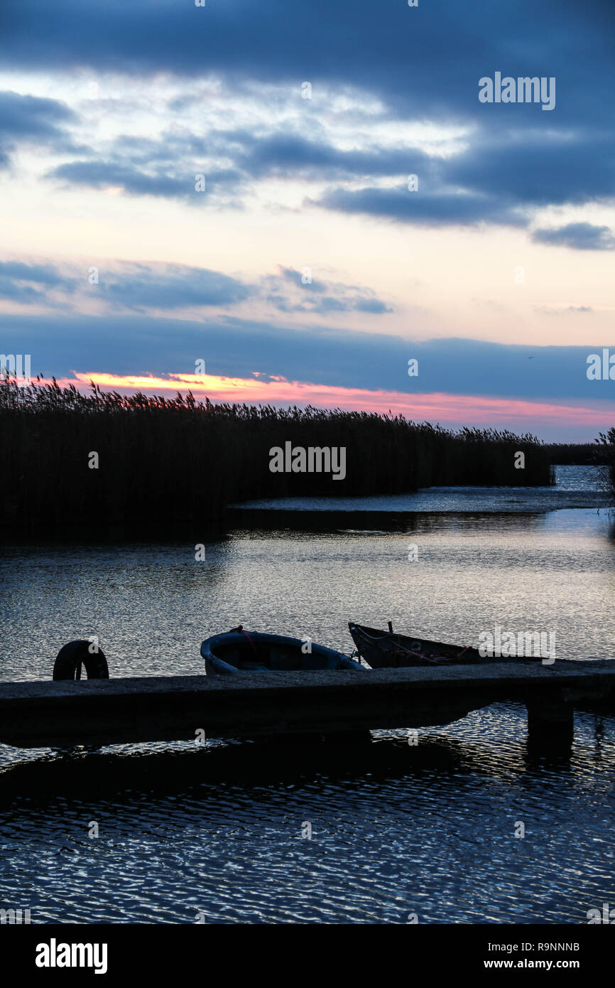 Sonnenuntergang Blick von der kleinen Dock, wo ein alter Wald angeln Boot schwimmt auf dem Wasser. Die Wolken sind auf dem Wasser wider. Stockfoto