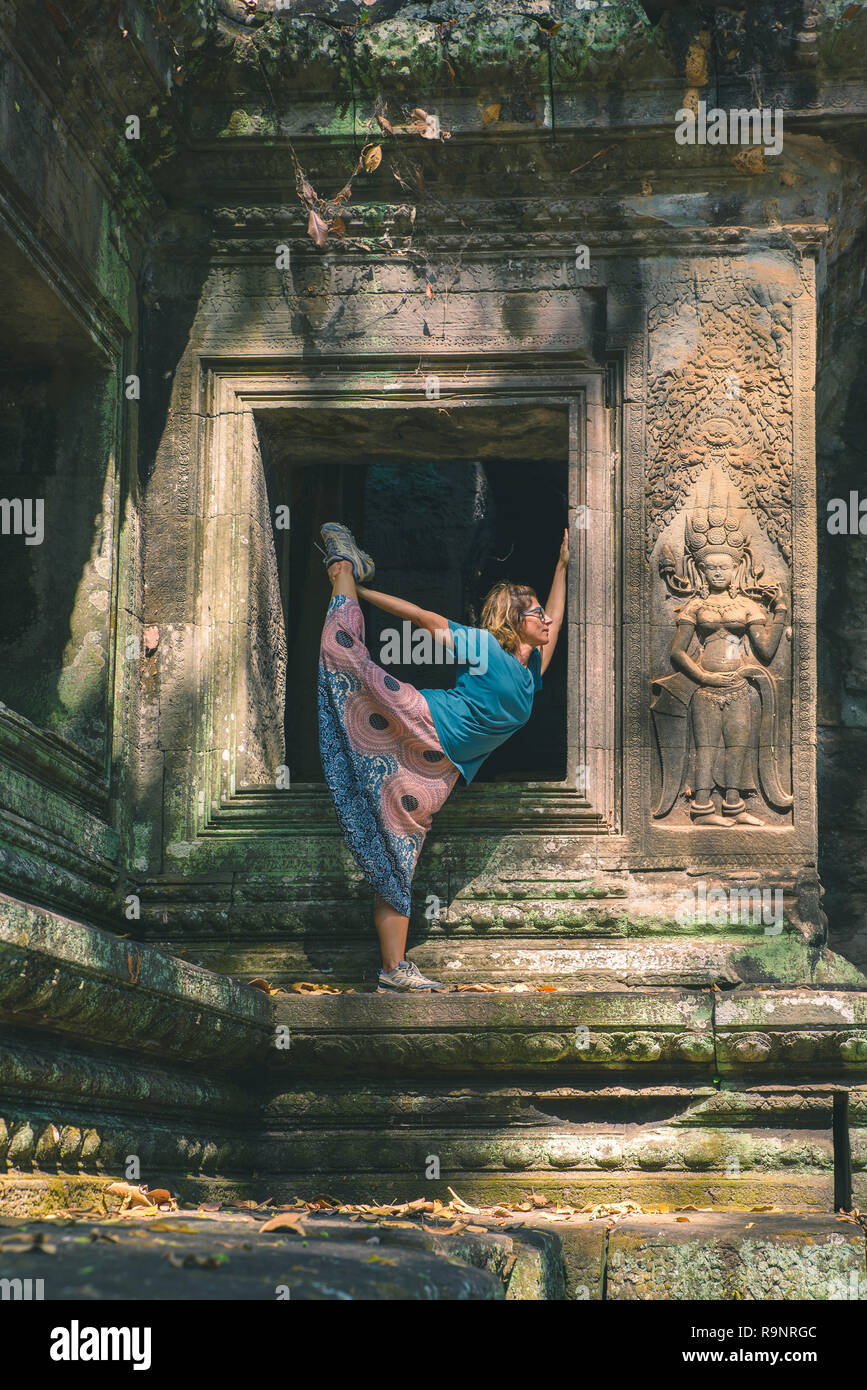 Eine Person in Angkor Wat Ruinen, Reiseziel Kambodscha. Frau in Yoga Position, Stretching Bein und hob den Arm, Profil ansehen, zwischen basreliefs ein Stockfoto