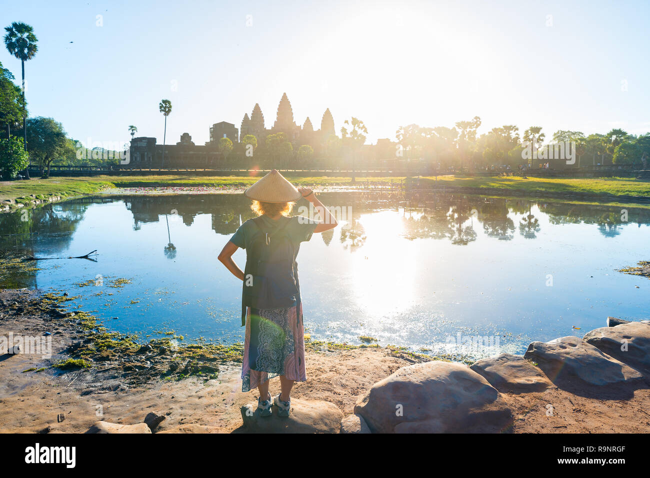 Eine touristische besuchen die Ruinen von Angkor Wat bei Sonnenaufgang, Reiseziel Kambodscha. Reflexion über Wasser Teich und sunburst, Frau mit traditionellen Hut und r Stockfoto