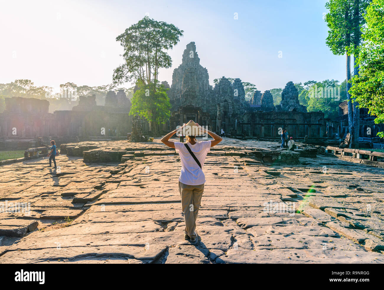 Einen touristischen Besuch Bayon Tempel, Angkor Thom Ruinen, Reiseziel Kambodscha. Frau mit traditionellen Hut und erhobenen Armen, Rückansicht, sunrise sunb Stockfoto