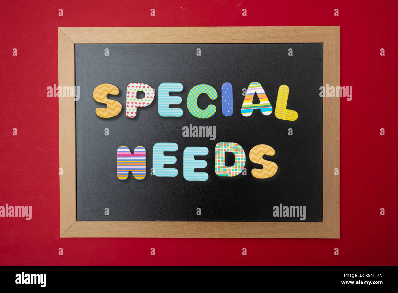 Schule besonderen Bedürfnissen Konzept. Schwarze Schiefertafel mit Holzrahmen, Text besondere Bedürfnisse in der bunte Buchstaben, rote Wand Hintergrund Stockfoto