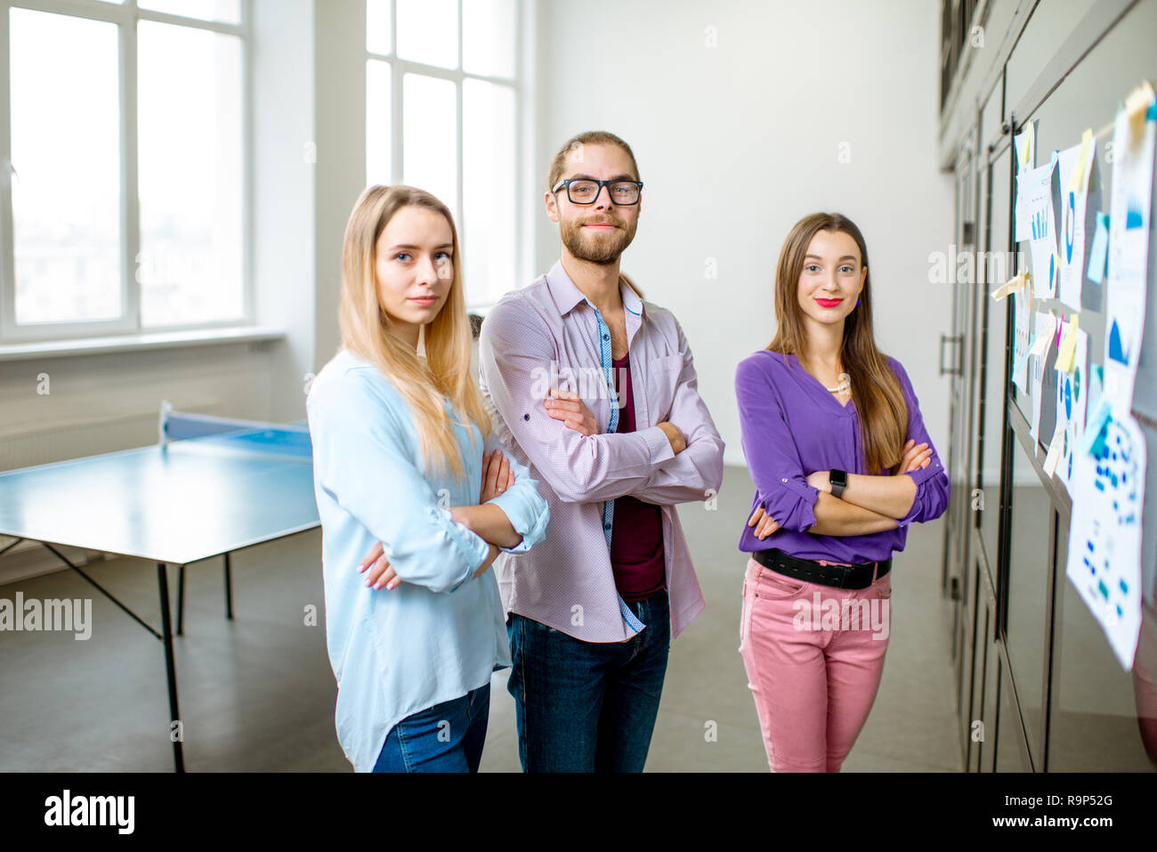 Porträt eines jungen Teams von Kollegen lässig gekleidet, stand in der Nähe der Glaswand mit einige Statistiken und Aufkleber im Büro Stockfoto