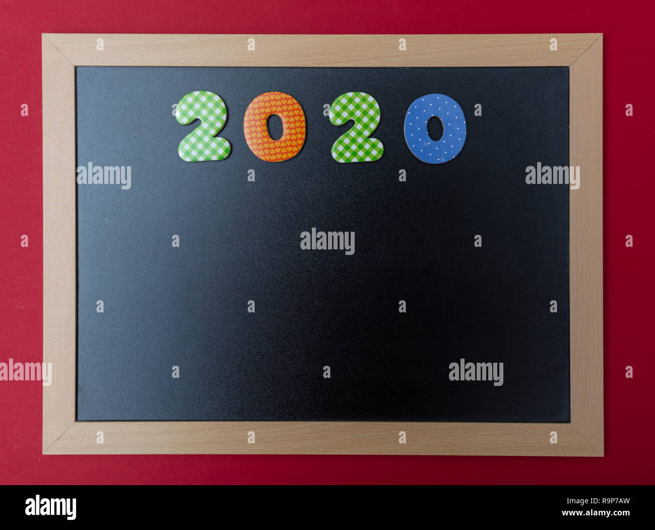 2020 für das neue Jahr. Schwarze Schiefertafel mit Holzrahmen, Nummer 2020 in bunten Zahlen, rote Wand Hintergrund, kopieren Raum Stockfoto