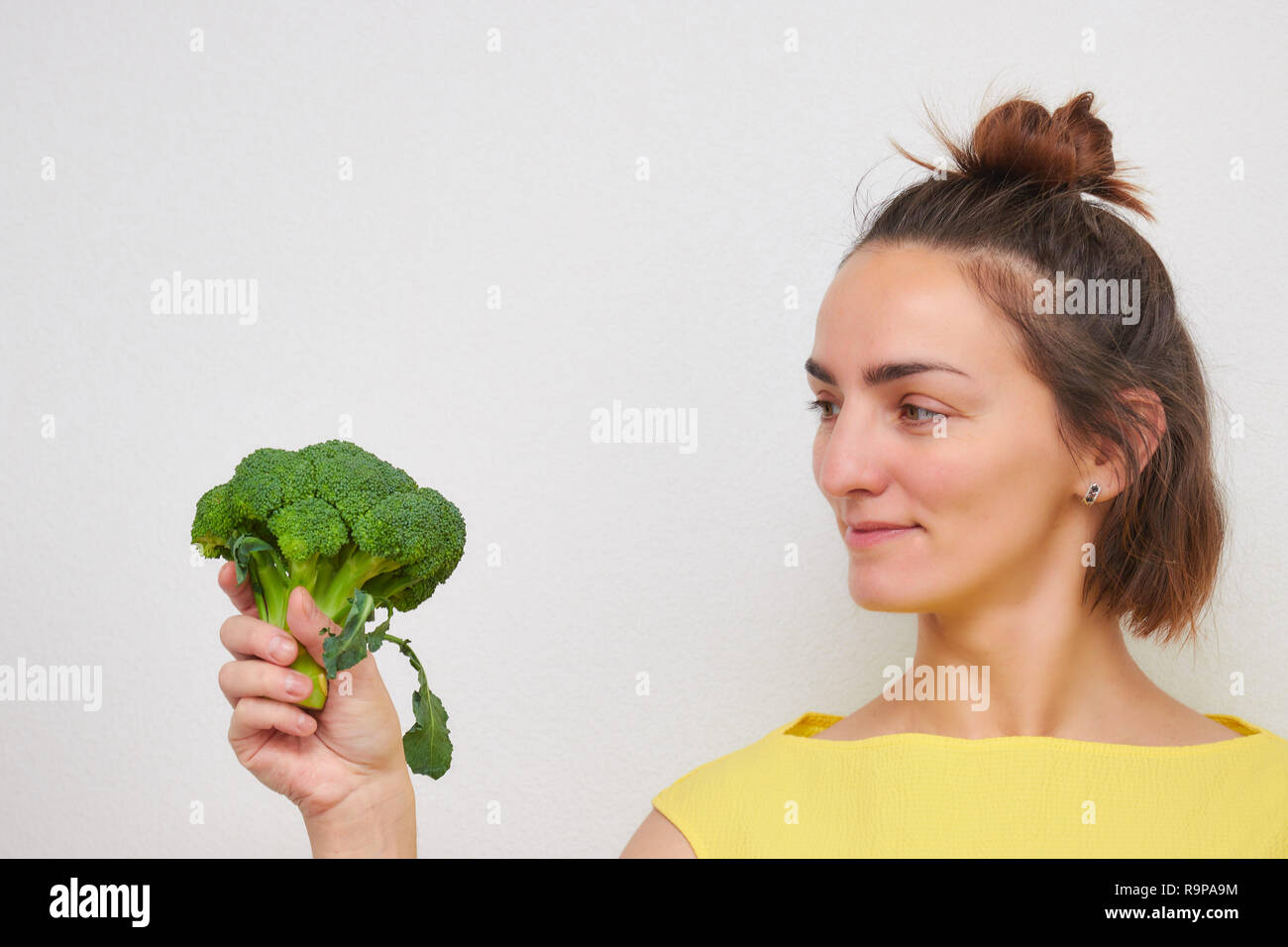Fröhliche, schöne, schlanke, Mädchen, dass Brokkoli Blütenstände in den Händen auf einem hellen Hintergrund isoliert. Frau der Europäischen aussehen. Stockfoto