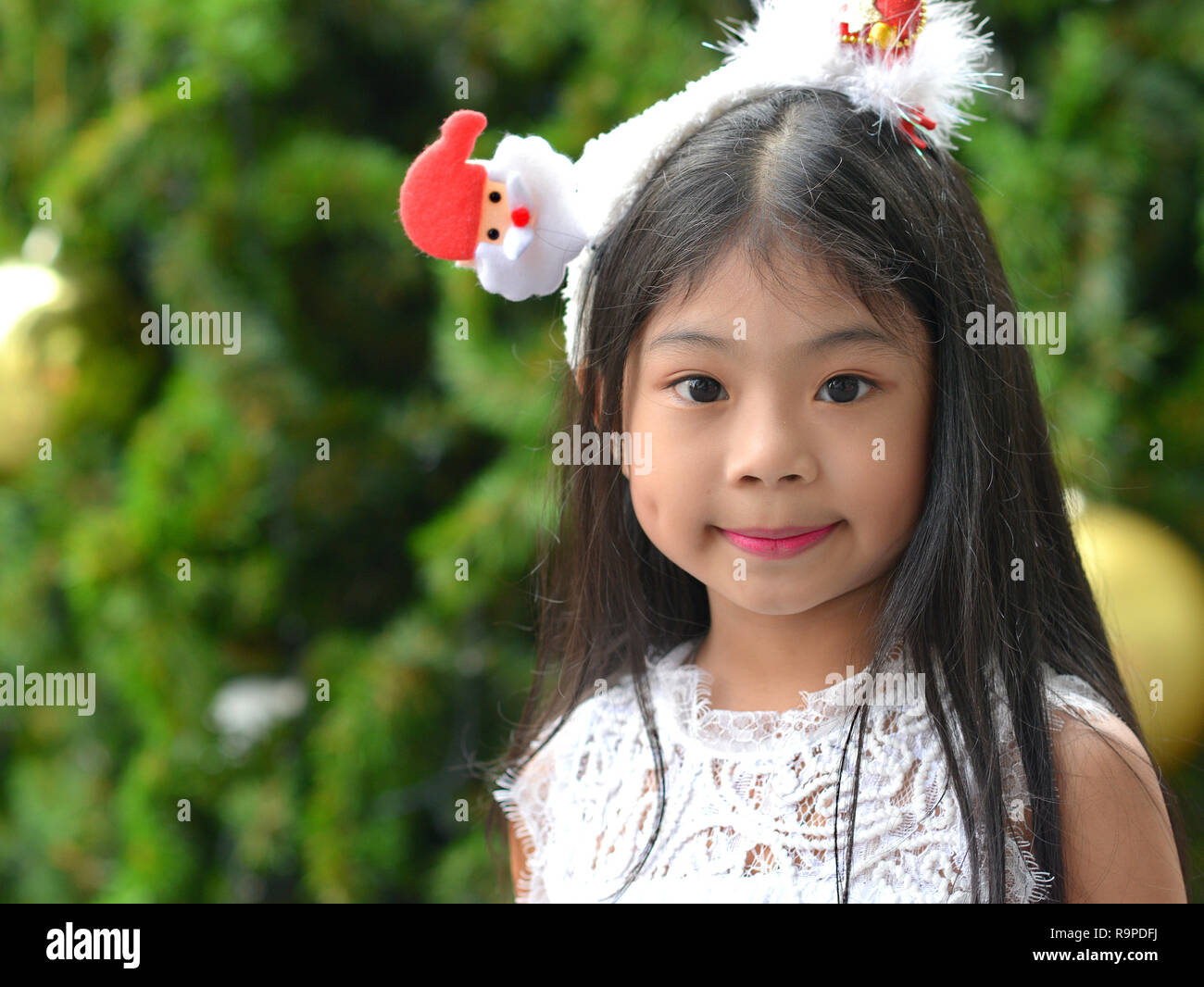 Süße kleine Thai Girl trägt einen traditionellen Weihnachtsmarkt Stirnband vor einem Weihnachtsbaum. Stockfoto