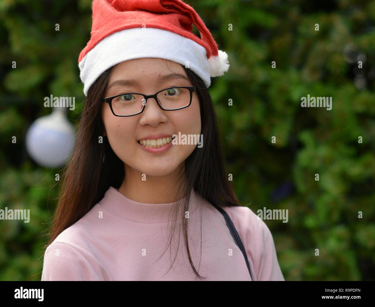 Hübsches Thai jugendlich Mädchen mit einem Weihnachtsmann hat ein Lächeln für die Kamera vor einem geschmückten Weihnachtsbaum. Stockfoto