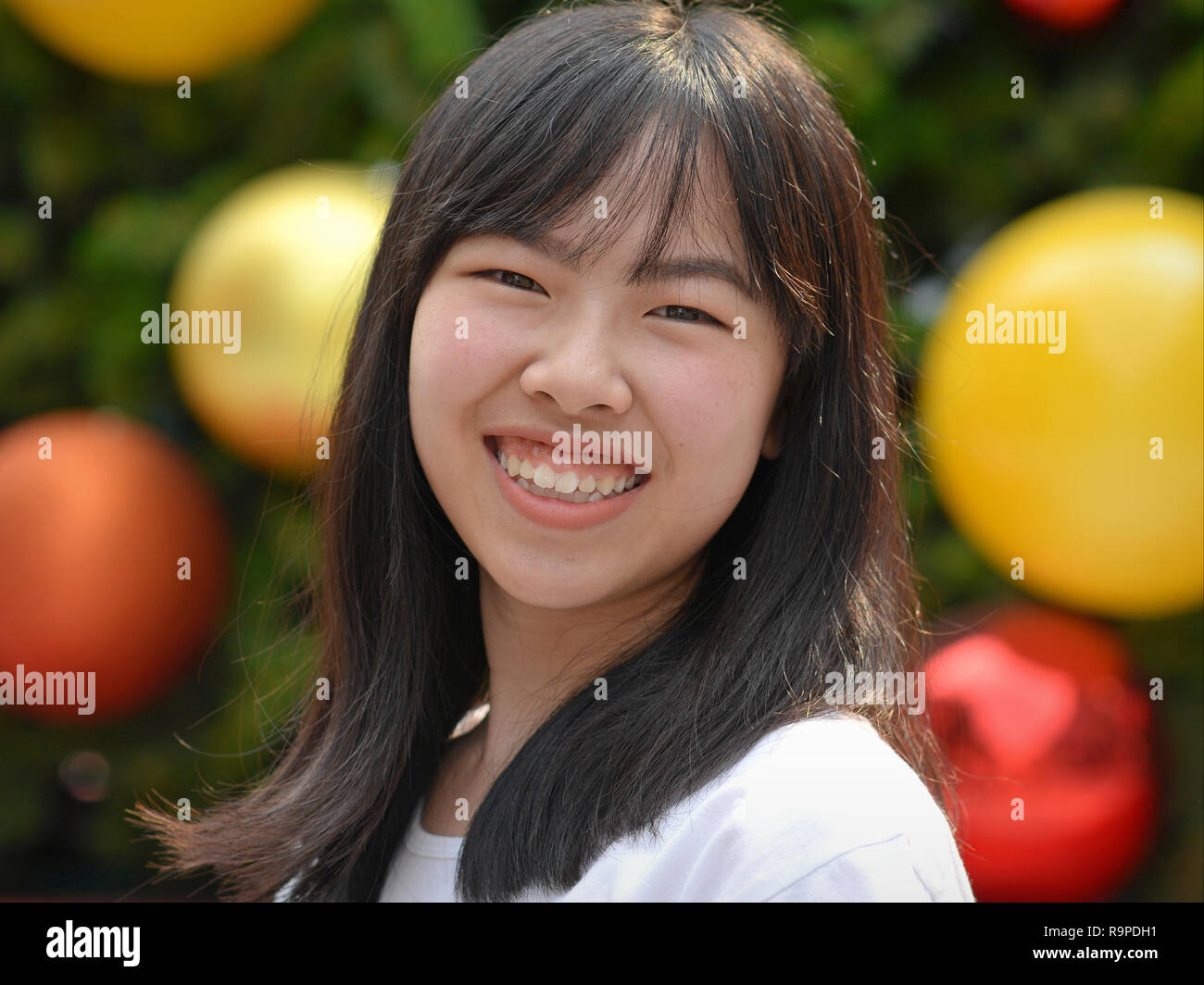 Thai Girl, Lächeln für die Kamera vor einem geschmückten Weihnachtsbaum. Stockfoto