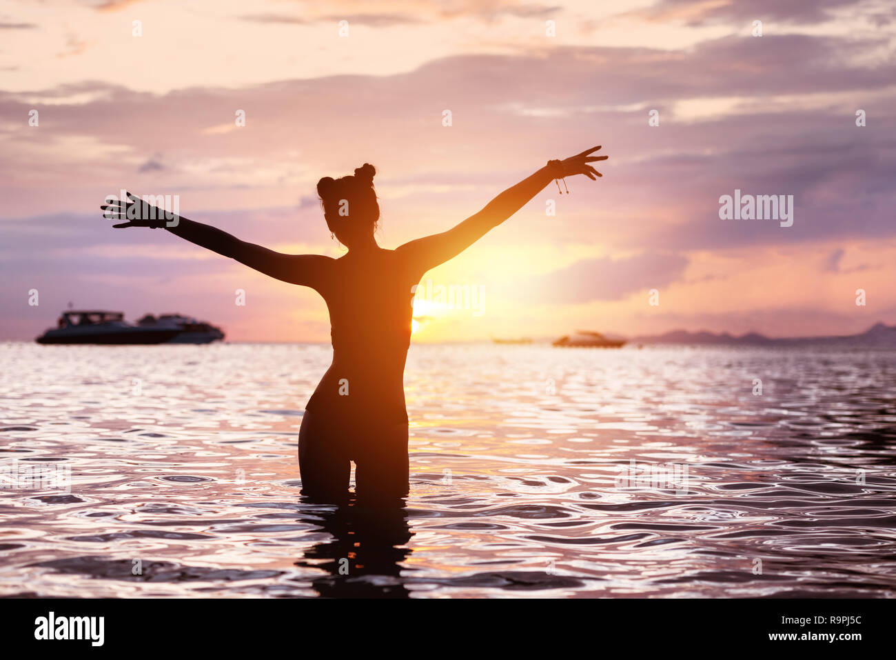 Silhouette der Glückliche schlanke Mädchen steht im ruhigen Wasser mit erhobenen Armen und Gruß Sonnenuntergang Stockfoto