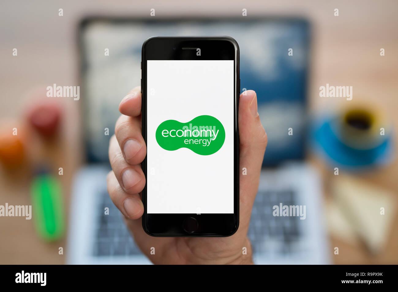 Ein Mann schaut auf seinem iPhone die zeigt die Wirtschaft Energie Logo (nur redaktionelle Nutzung). Stockfoto