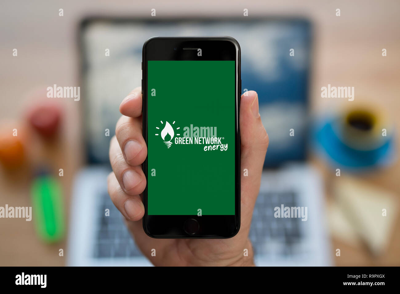 Ein Mann schaut auf seinem iPhone die zeigt das Grüne Netzwerk Energie Logo (nur redaktionelle Nutzung). Stockfoto