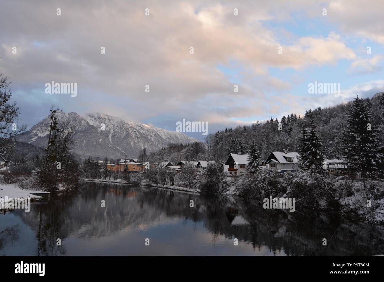 Kleine Häuser am Ufer des Flusses, verschneite Berge und malerischen Sky im Hintergrund. Bad Goisern, Hallstatt, Österreich. Winter Blick auf den Fluss. Stockfoto