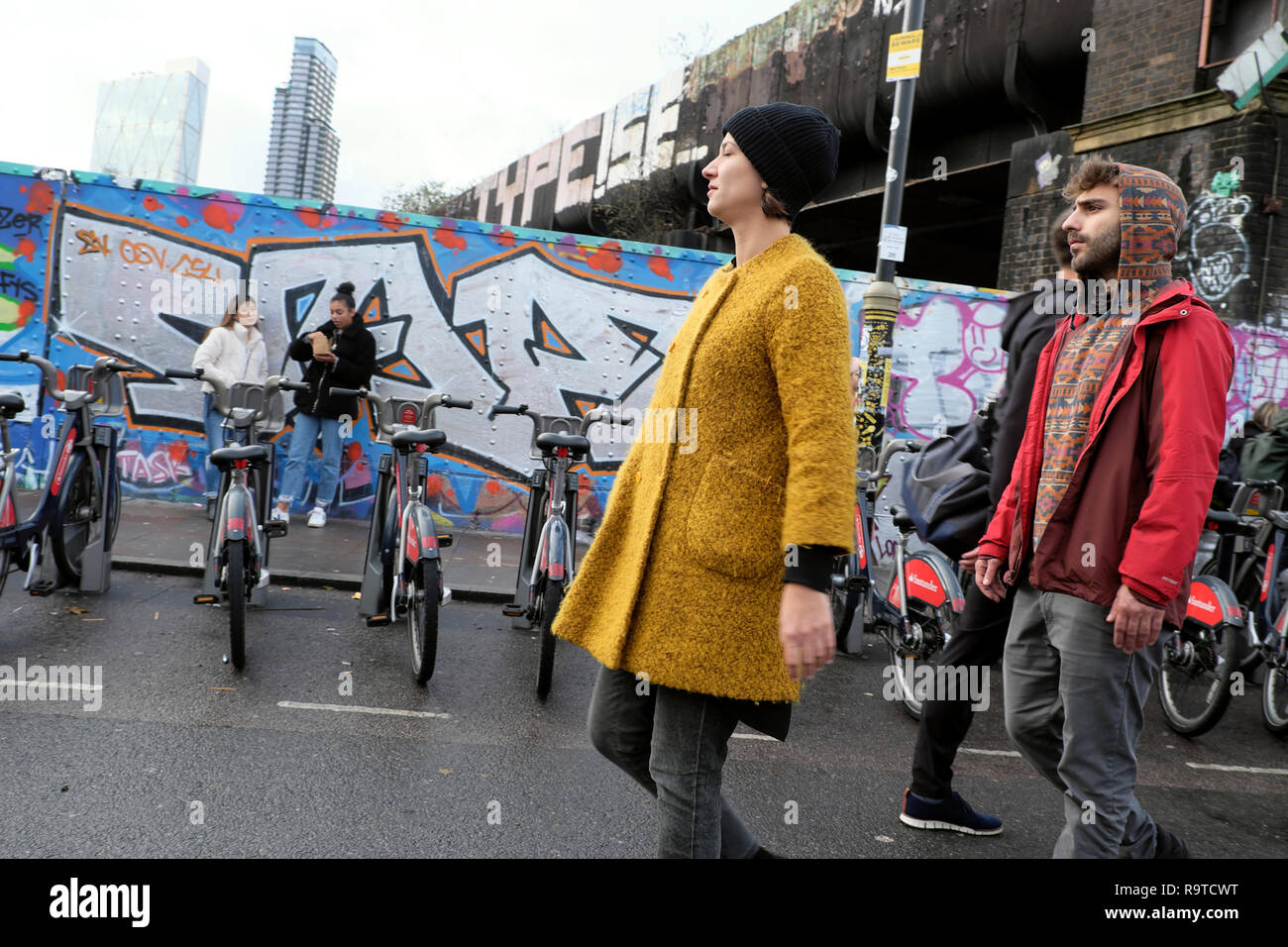 Die Leute, die Brick Lane East End junge Frau tragen gelbe Fell die Straße entlang bummeln in Winter in Shoreditch East London E1 UK KATHY DEWITT Stockfoto
