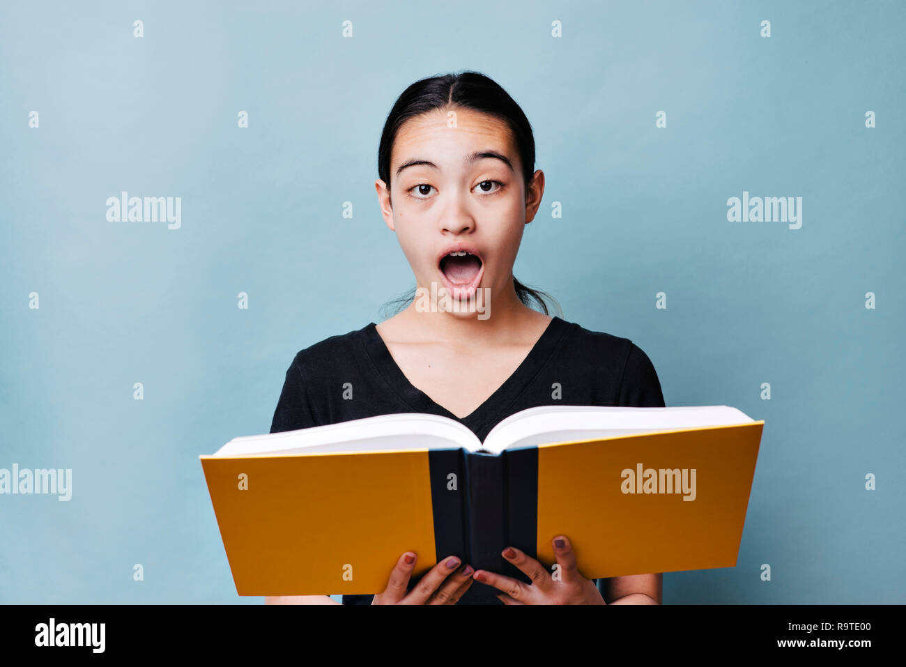 Junge Schülerin liest Lehrbuch und hat eine schockierte Ausdruck Stockfoto