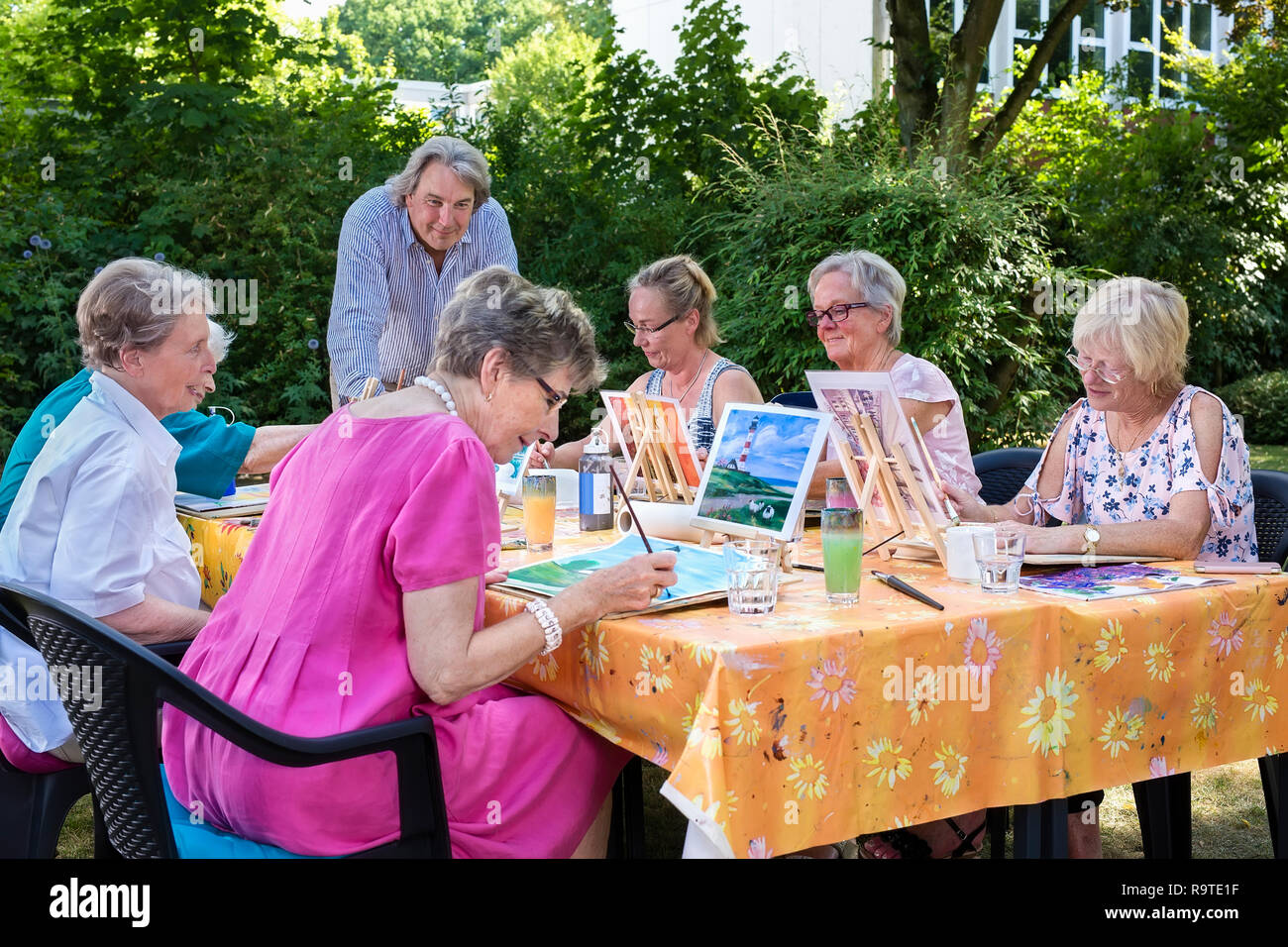 Älteren Damen die Kunst Unterricht im Freien sitzen am Tisch und malen Bilder, folgenden männliche Lehrer. Stockfoto