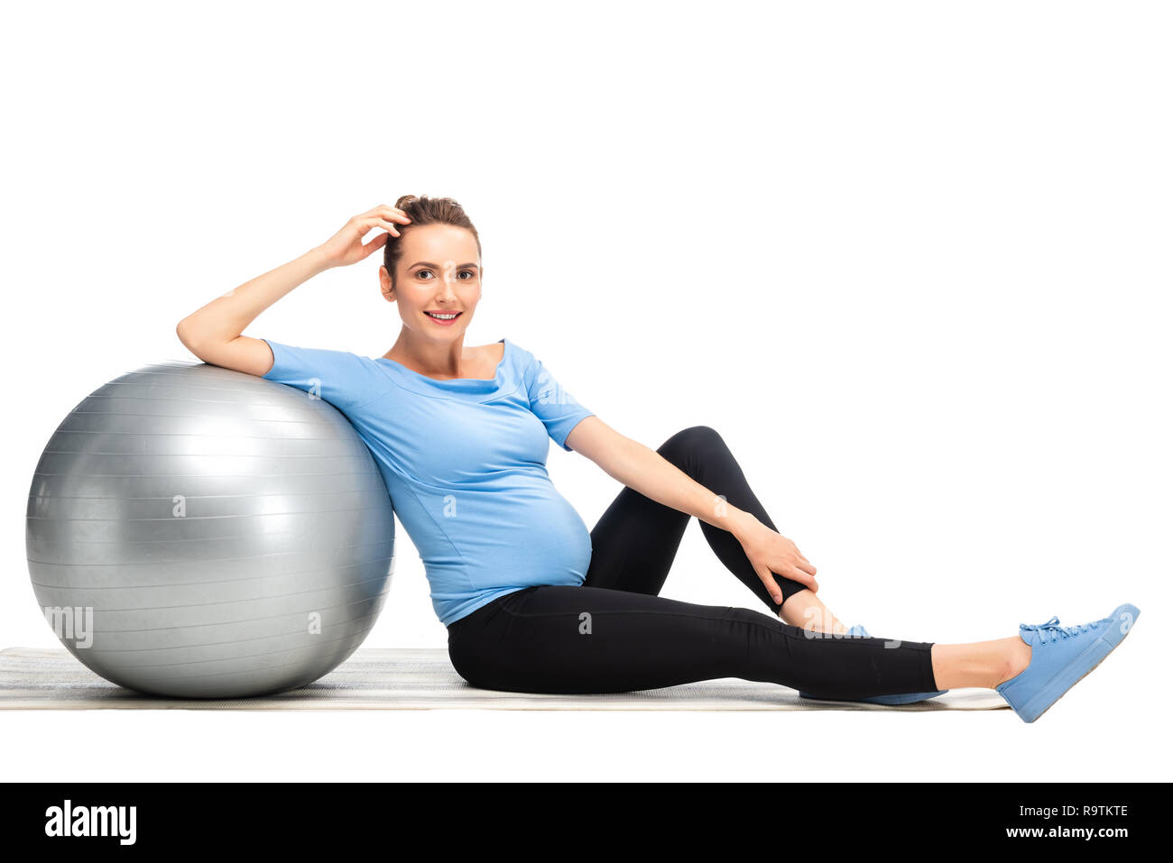 Braune behaarte schwangere Frau sitzt auf dem Boden mit grauen Fitness Ball isoliert auf weißem Stockfoto