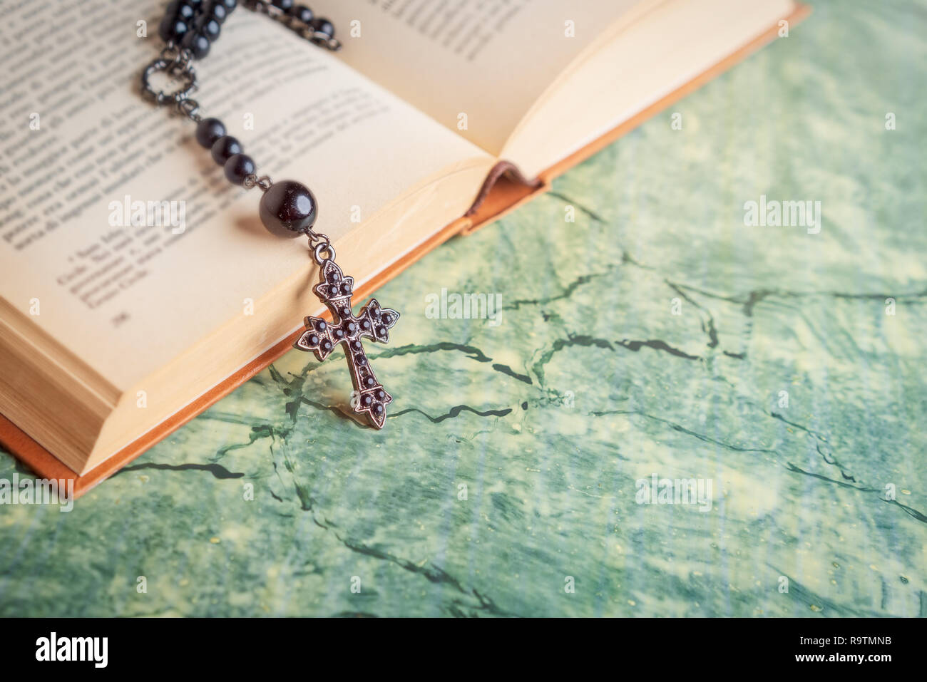 Schwarz Rosenkranz und Kreuz auf die Bibel auf einem grünen Tisch. Religion in der Schule. Stockfoto