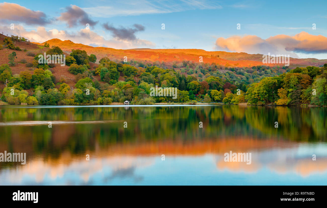 Herbstlicher Sonnenuntergang über dem Spiegelbild im Wasser in Richtung Rydal Boat House & die goldene Berge in der Ferne suchen. Stockfoto